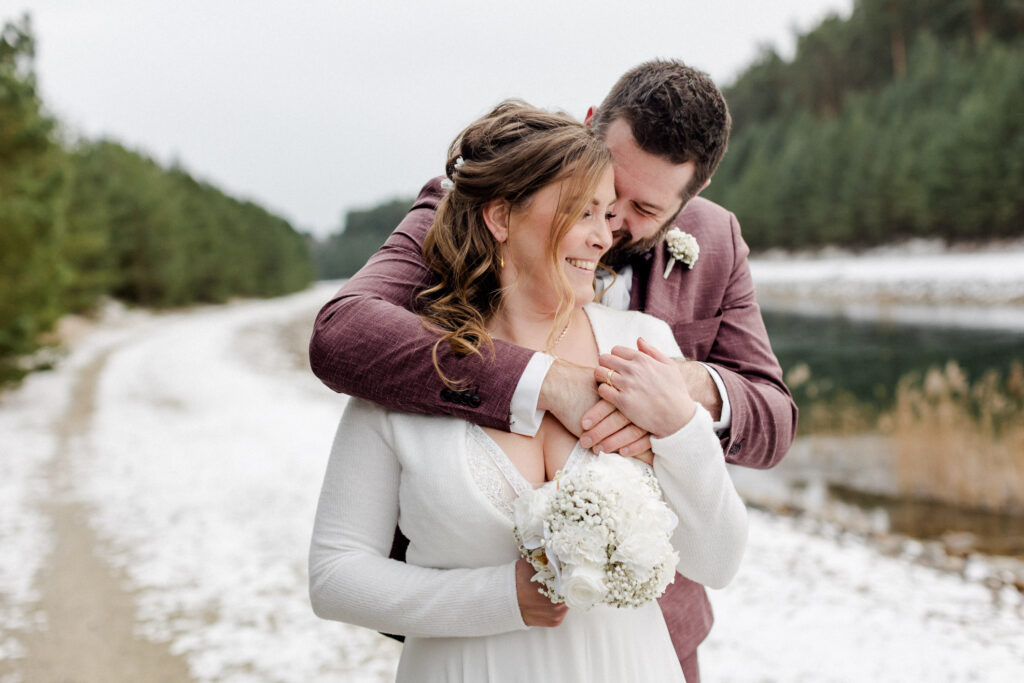 Braut und Bräutigam spazieren eng umschlungen im Schnee – winterliche Hochzeit für einen Hochzeitsfilm in Dresden